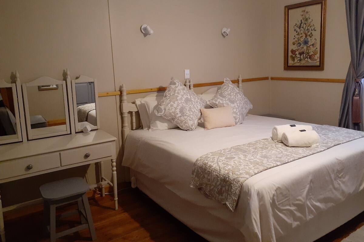 Ein ordentlich eingerichtetes Schlafzimmer mit Bett, Nachttisch, Spiegel und einem Bild an der Wand.