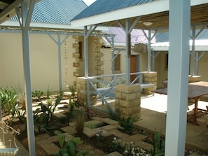 A covered outdoor area with a patio table and chairs, surrounded by stone planters and greenery. - Sandstone Chameleon Guesthouse Fouriesburg (Fouriesburg)