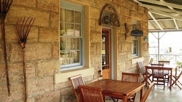 A stone building with a wooden table and chairs, a window, and a door. - Sandstone Chameleon Guesthouse Fouriesburg (Fouriesburg)