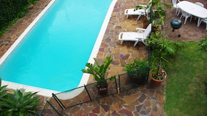 A swimming pool with a stone border, surrounded by potted plants and white lounge chairs.