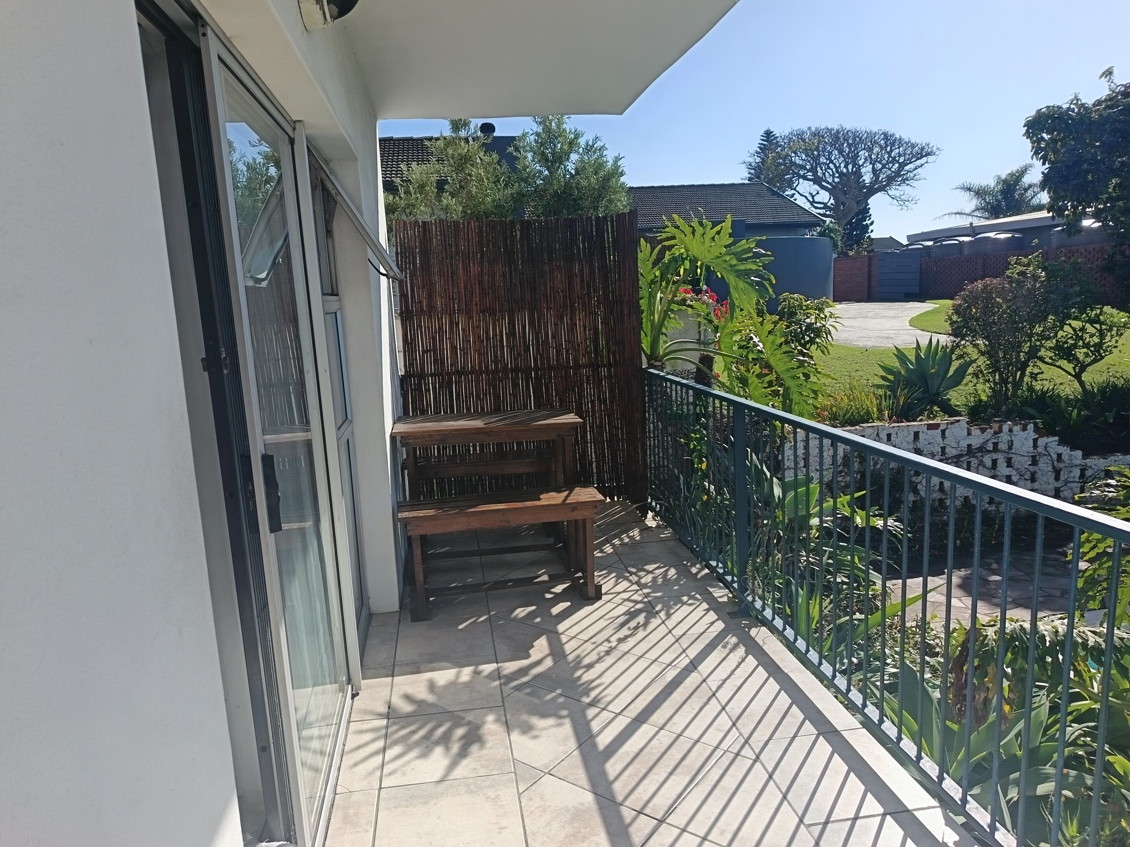 A balcony with a view of a garden, a wooden bench, and a metal railing.