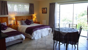 A bedroom with two beds, a dining table with chairs, and a balcony with a railing.