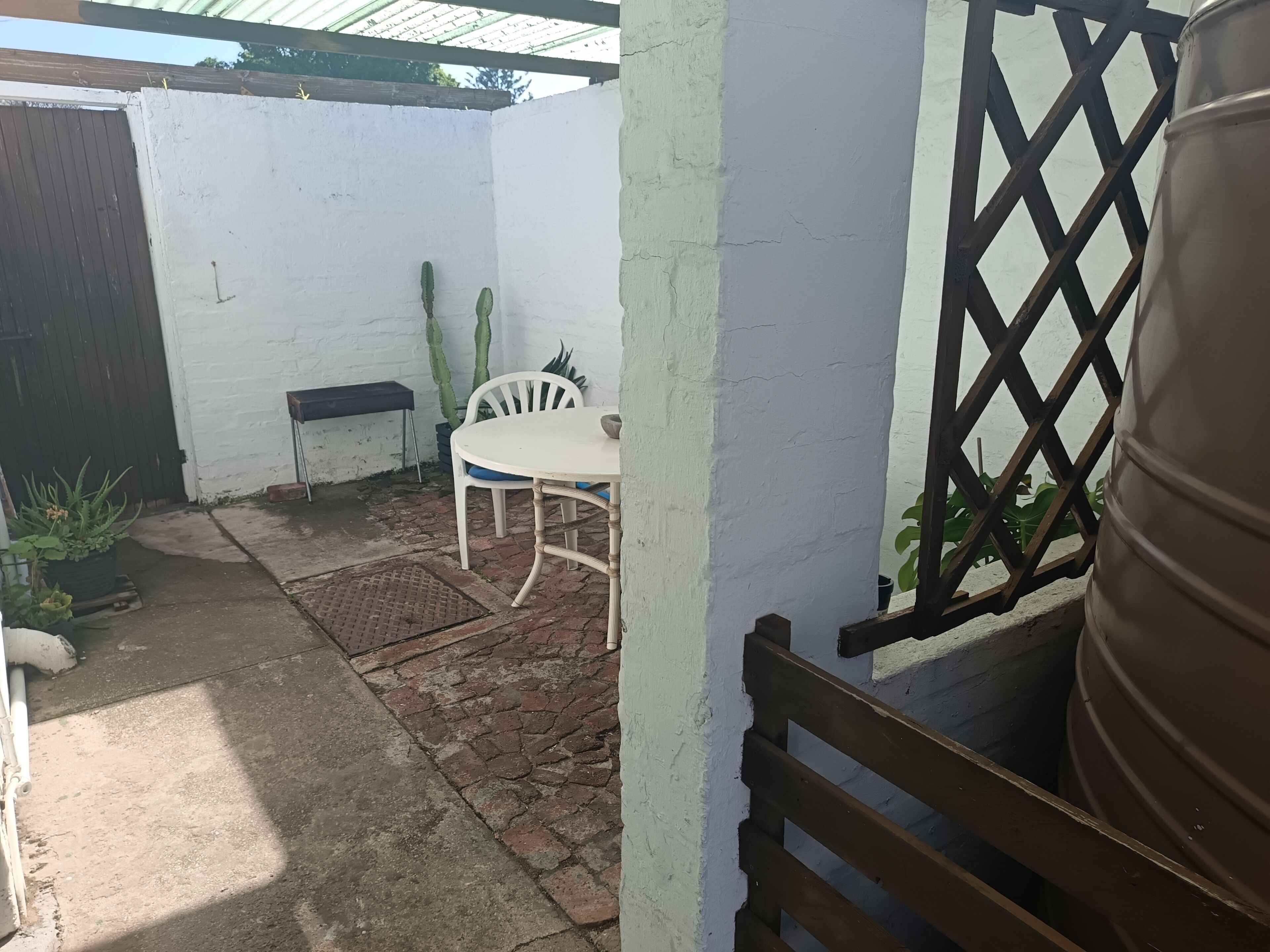 A patio area with a white table and chairs, a potted plant, and a metal barrel.