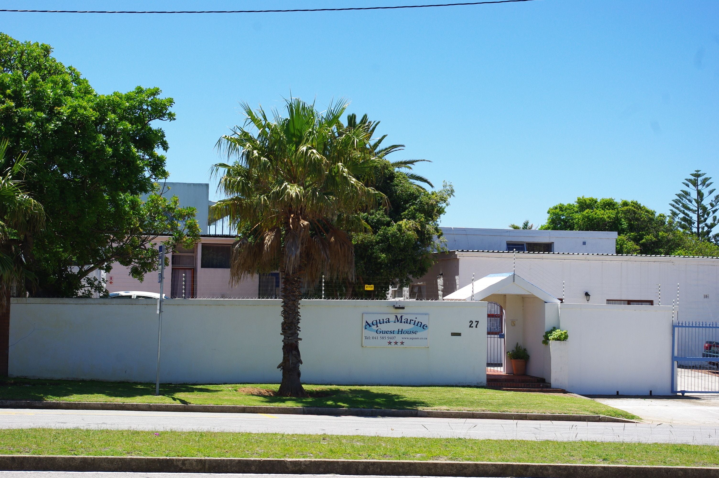 A guest house named Aqua Marine with a white exterior, a palm tree in front, and a clear blue sky.