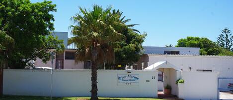 A guest house named Aqua Marine with a white exterior, a palm tree in front, and a clear blue sky.