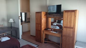 Kompakti hotellihuone, jossa on sänky, työpöytä ja televisio, ruokailutila sekä pieni keittiönurkkaus.