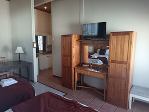 Quarto de hotel compacto com cama, escrivaninha com televisão, espaço de refeições e cozinha compacta.