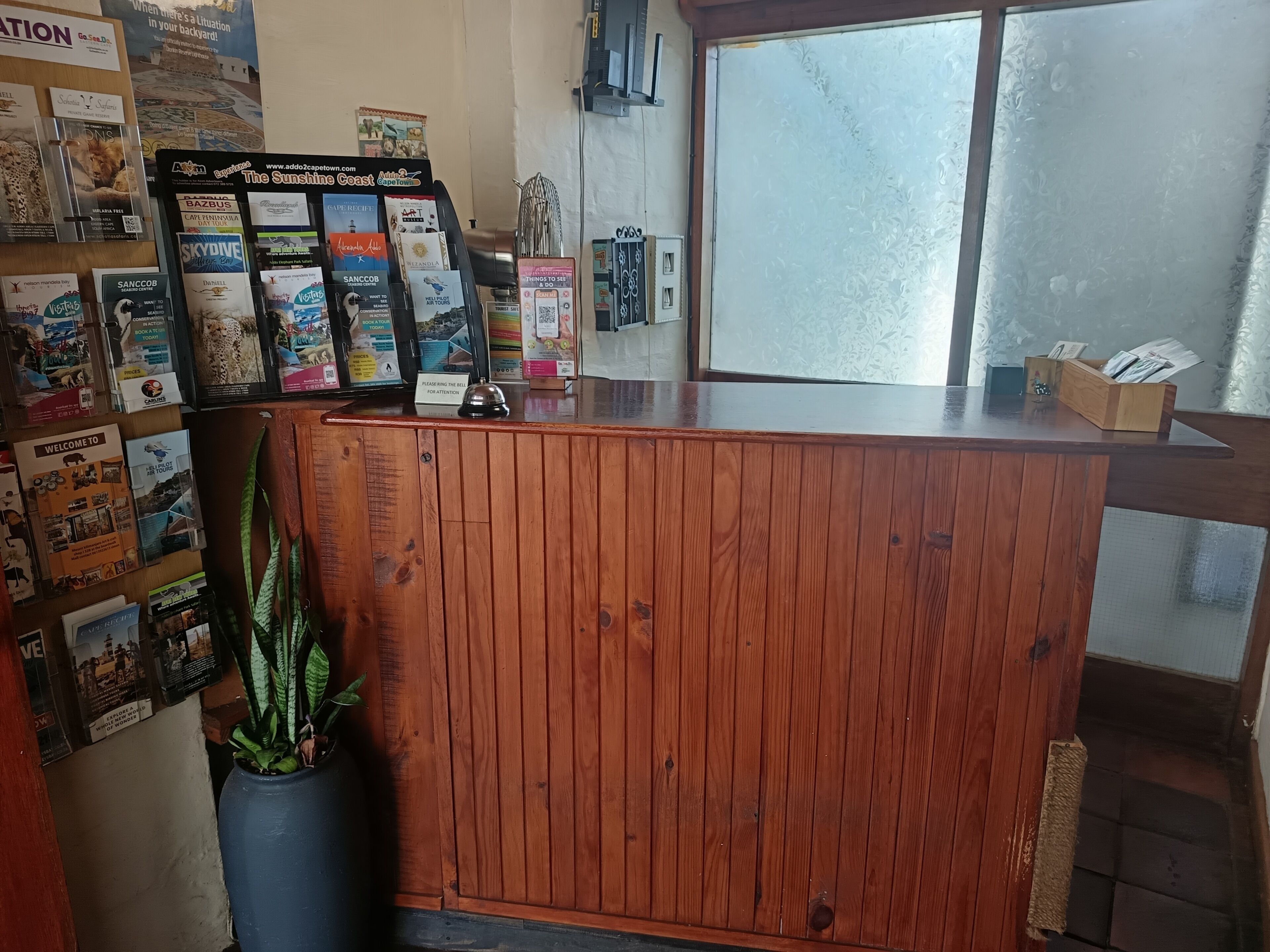 En receptionsdisk med träpanel, omgiven av olika broschyrer om resmål och en krukväxt.