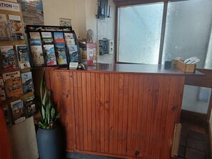 Een receptiebalie met houten afwerking, omringd door diverse reisbrochures en een plant in pot.