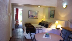 A cozy room with a bed, bedside table, lamp, and a small round table with a plant.