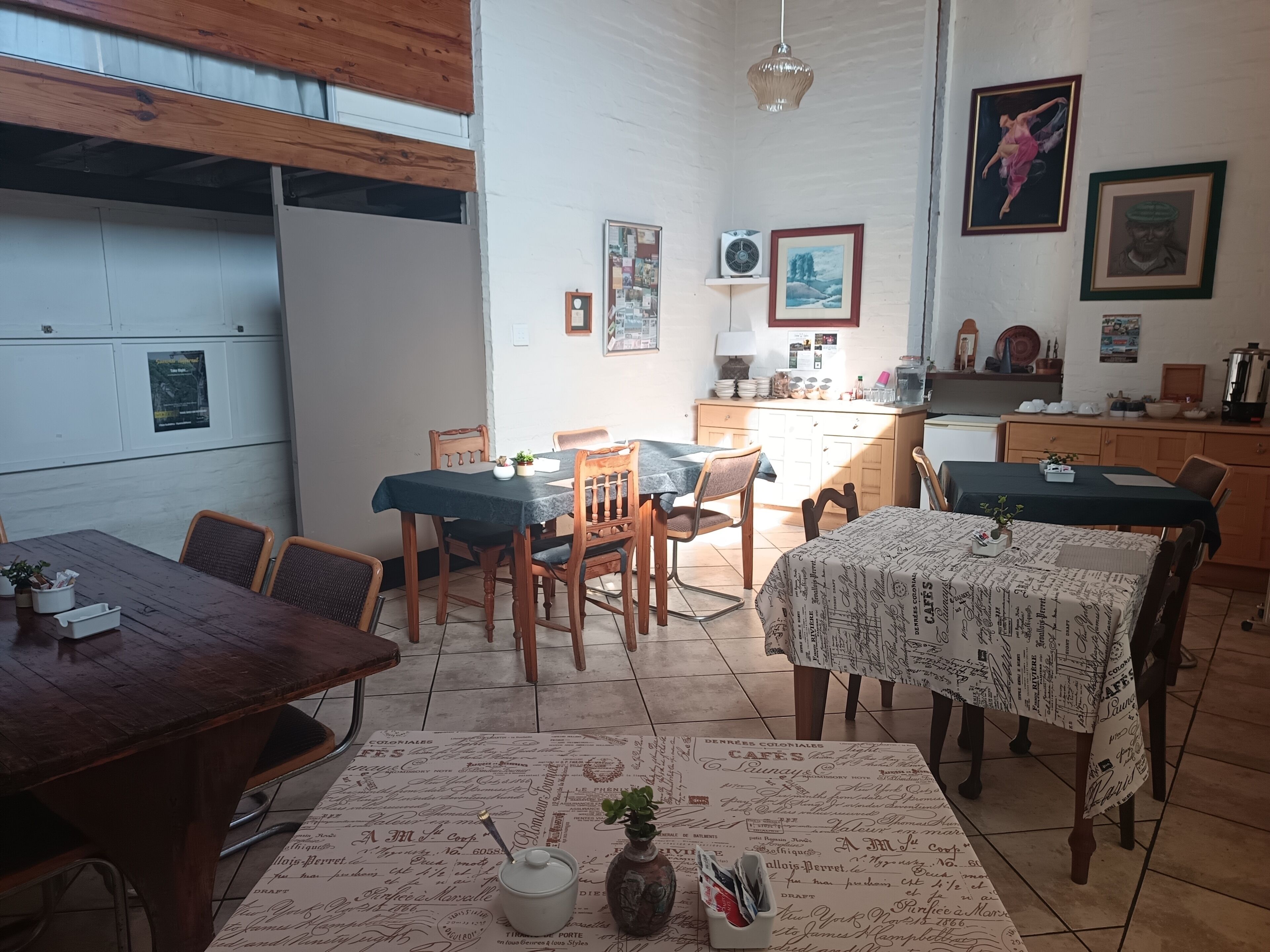 A dining area with wooden tables and chairs, a kitchen in the background, and various wall decorations.
