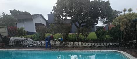 A swimming pool with a stone tile border, surrounded by a stone wall and vegetation.