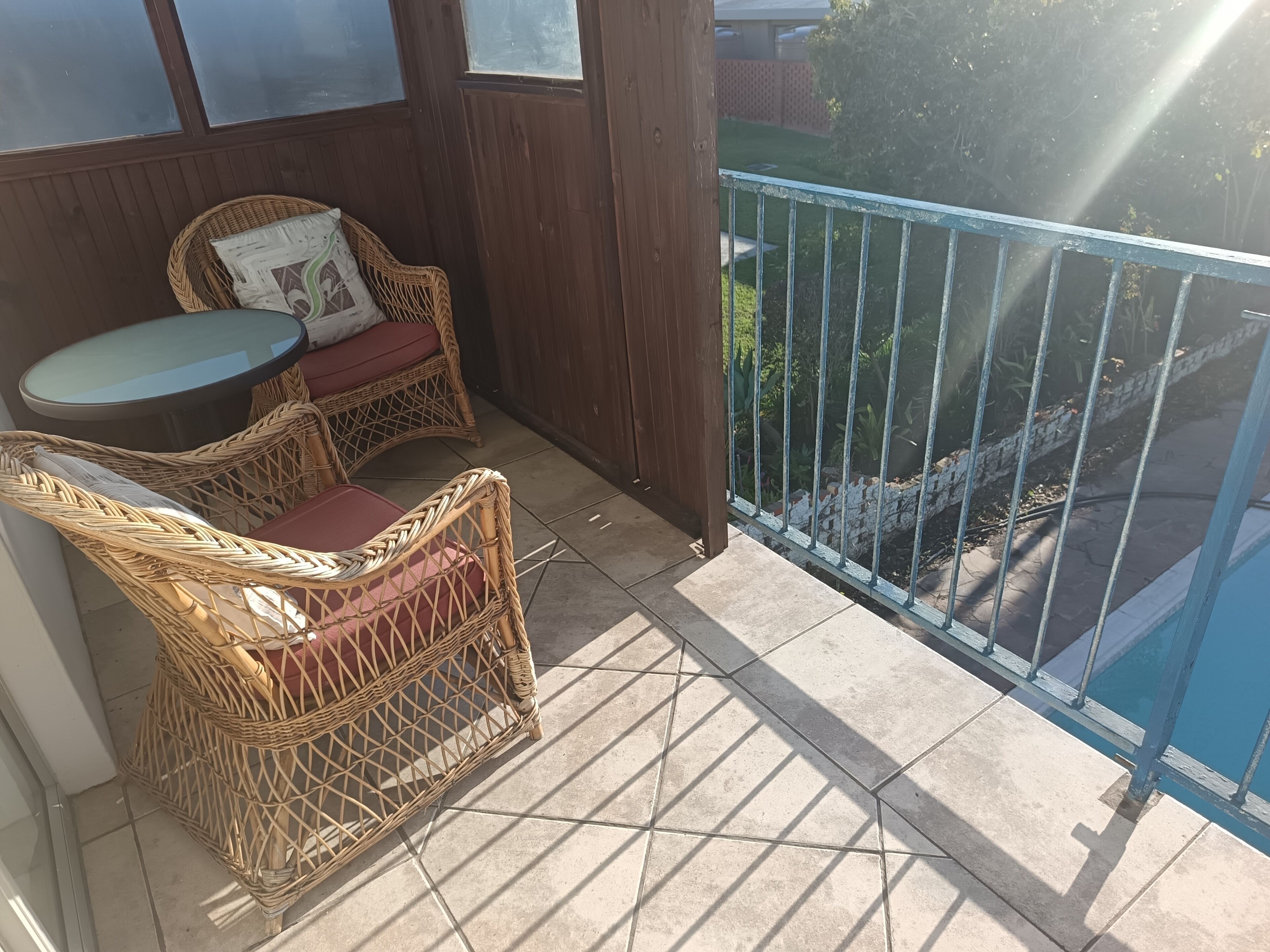 A balcony with wicker furniture, a small table, and a view of a garden.