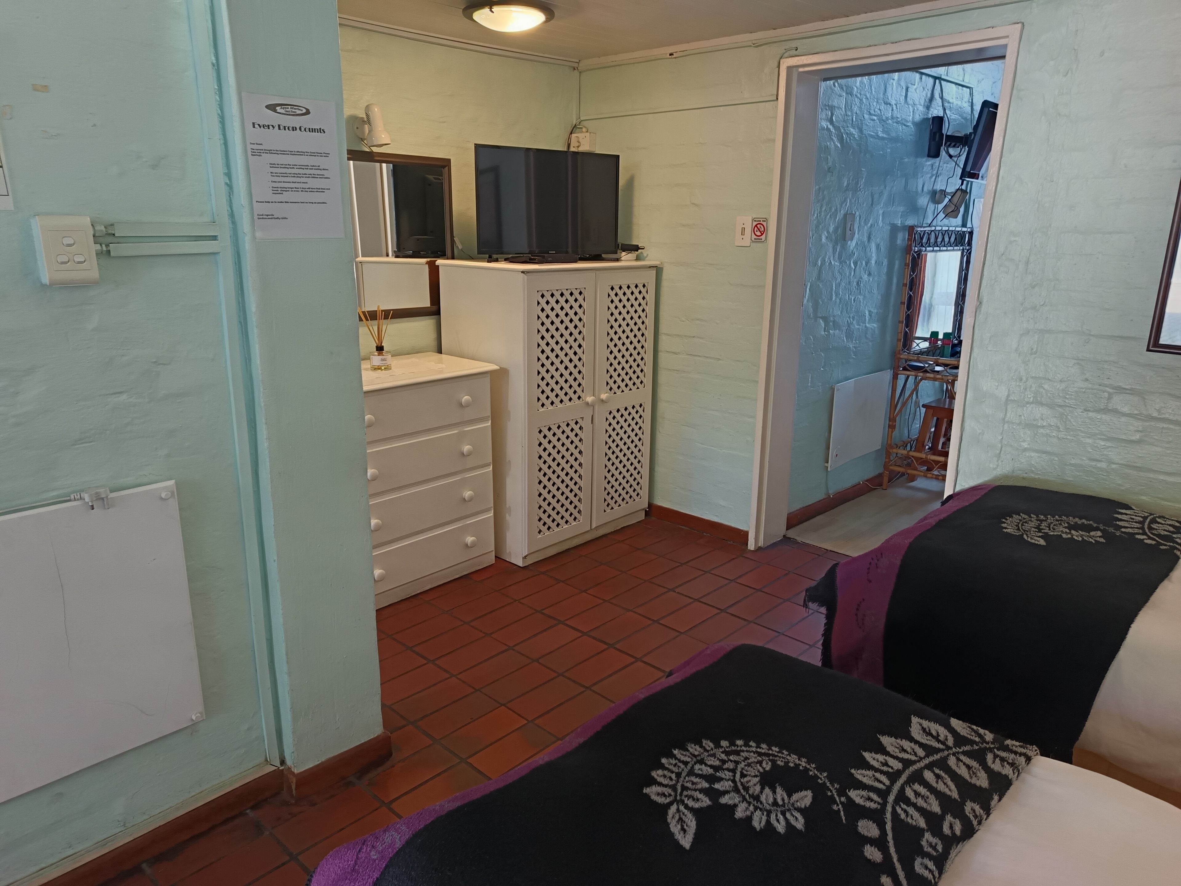 Quarto com cama, cômoda, televisão e porta que dá para outro espaço.