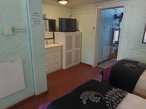 A room with a bed, a dresser, a television, and a door leading to another room.