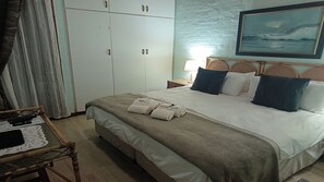 Een hotelkamer met een bed, nachtkastje, lamp, schilderij aan de muur en een kledingkast.