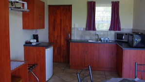 A compact kitchen with wooden cabinets, a refrigerator, a microwave, and a small sink.