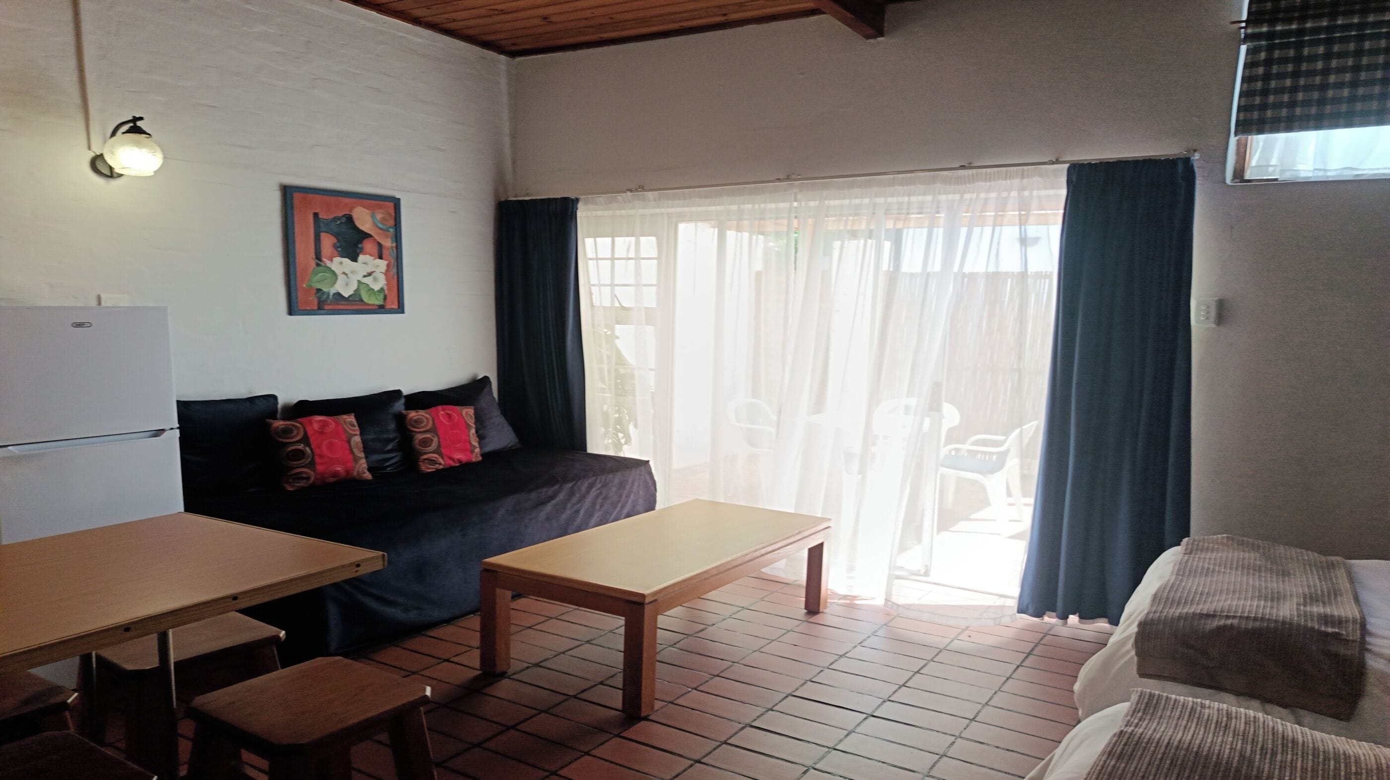 A compact living space with a kitchenette, a sofa with patterned cushions, a dining table, and a sliding glass door leading to an outdoor area.