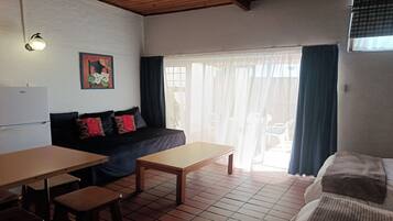 A compact living space with a kitchenette, a sofa with patterned cushions, a dining table, and a sliding glass door leading to an outdoor area.