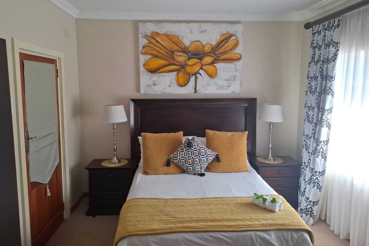 A hotel room with a bed, two nightstands, a painting above the bed, and a door on the left.