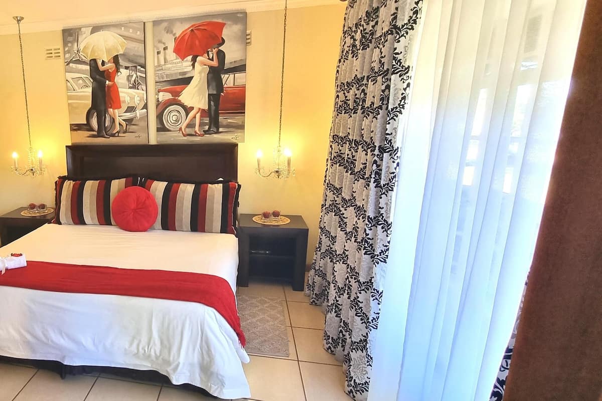 A bedroom with a bed, a wardrobe, a painting, two bedside tables, and a chandelier.