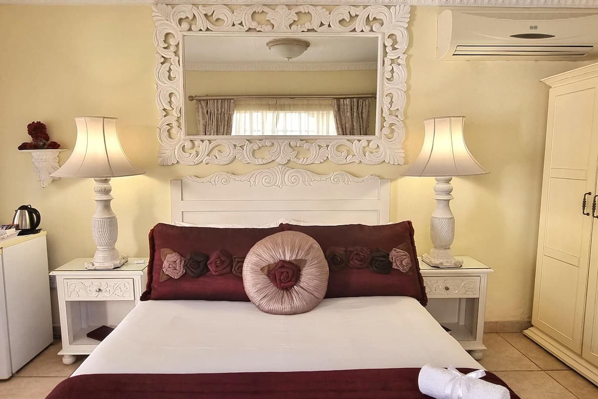 A hotel room with a bed, two bedside lamps, a dresser, a mirror, and a wardrobe.