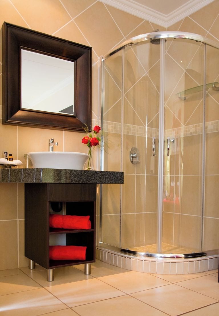 Un baño moderno con cabina de ducha de vidrio curvo, tocador con lavamanos y espejo superior.