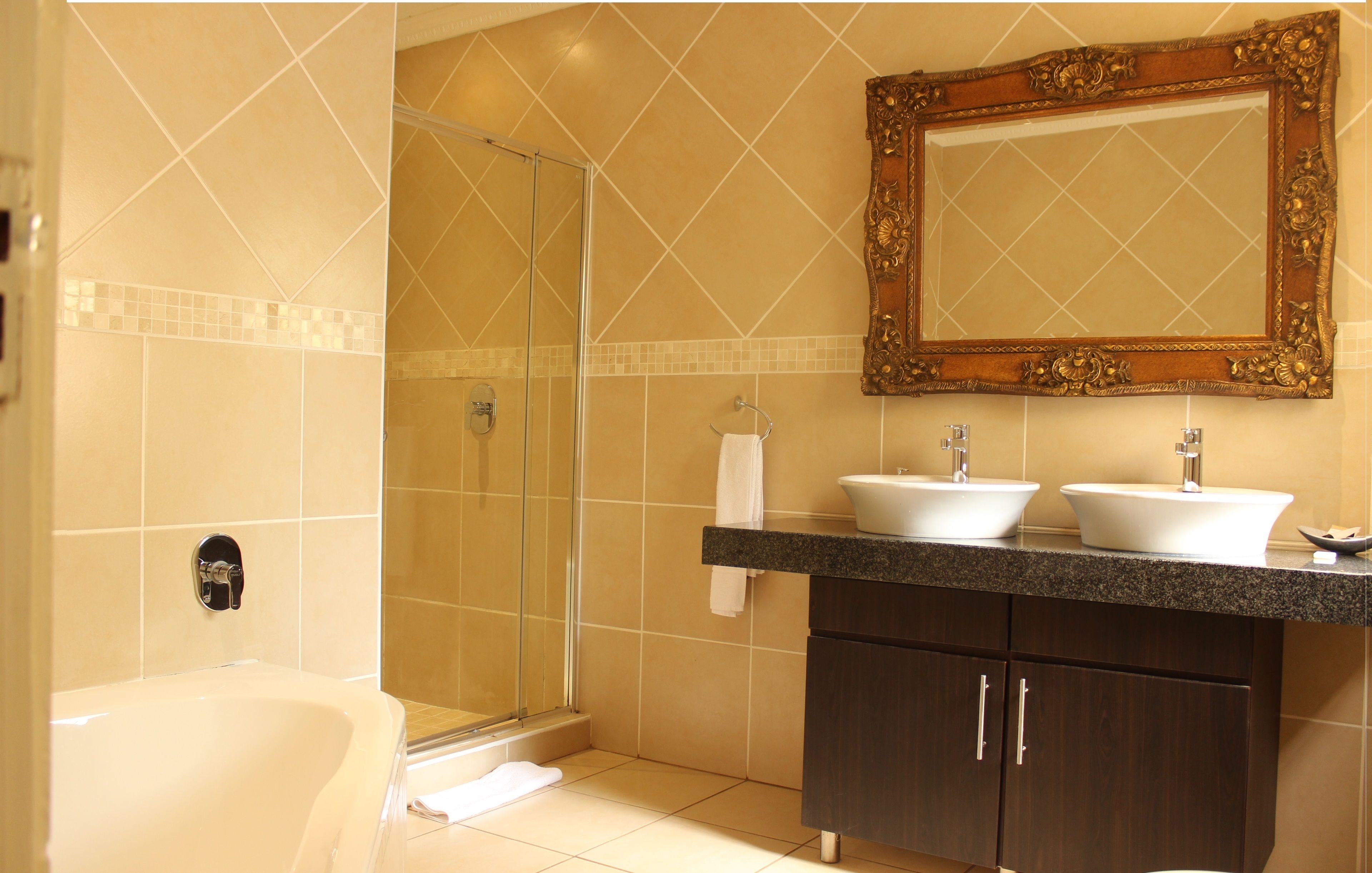 Une salle de bain dotée d’une douche à parois de verre, de deux lavabos, d’un grand miroir et de meubles de rangement aux couleurs sombres.