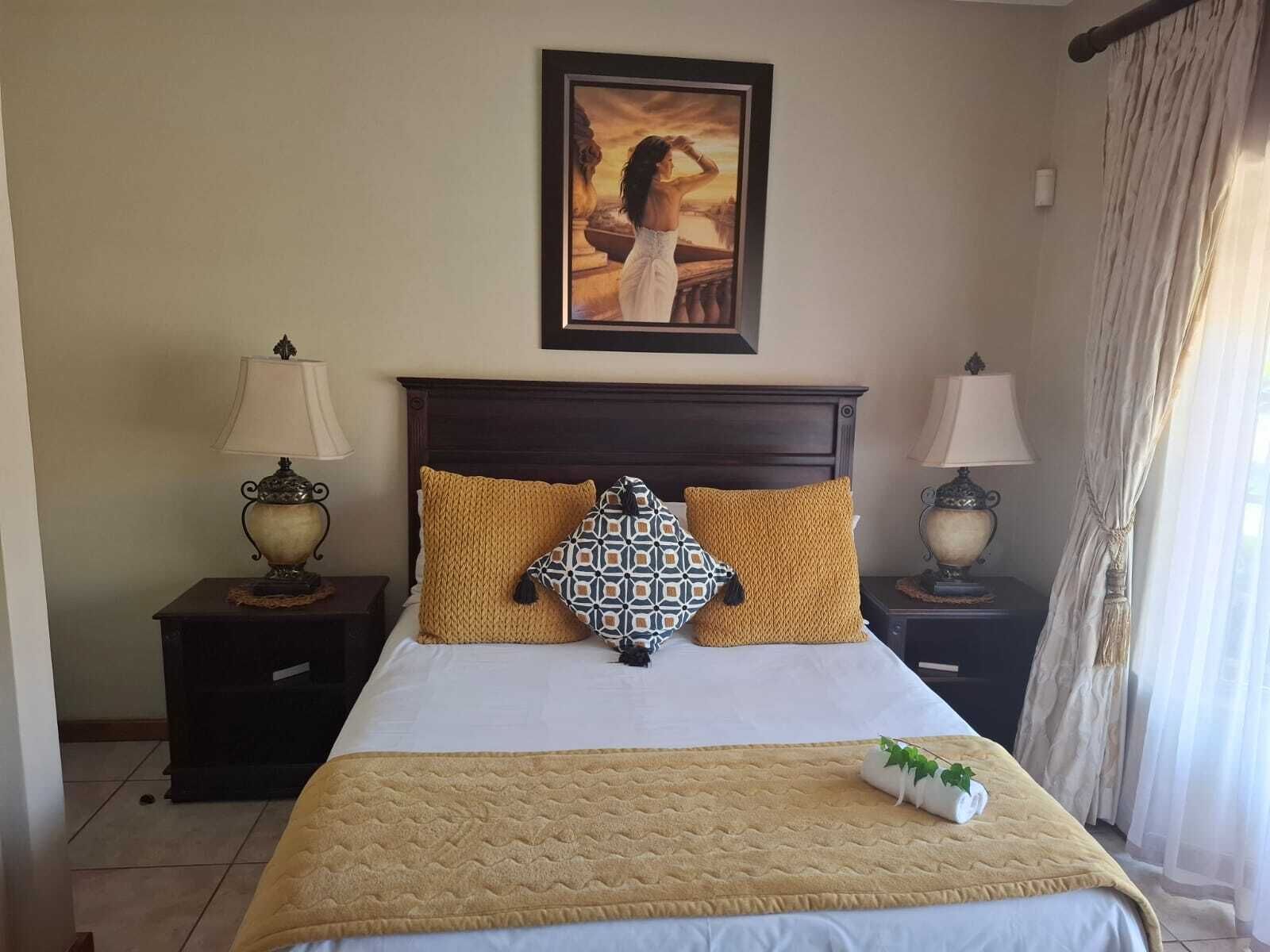 A hotel room with a large bed, two nightstands with lamps, a painting above the bed, and a window with curtains.