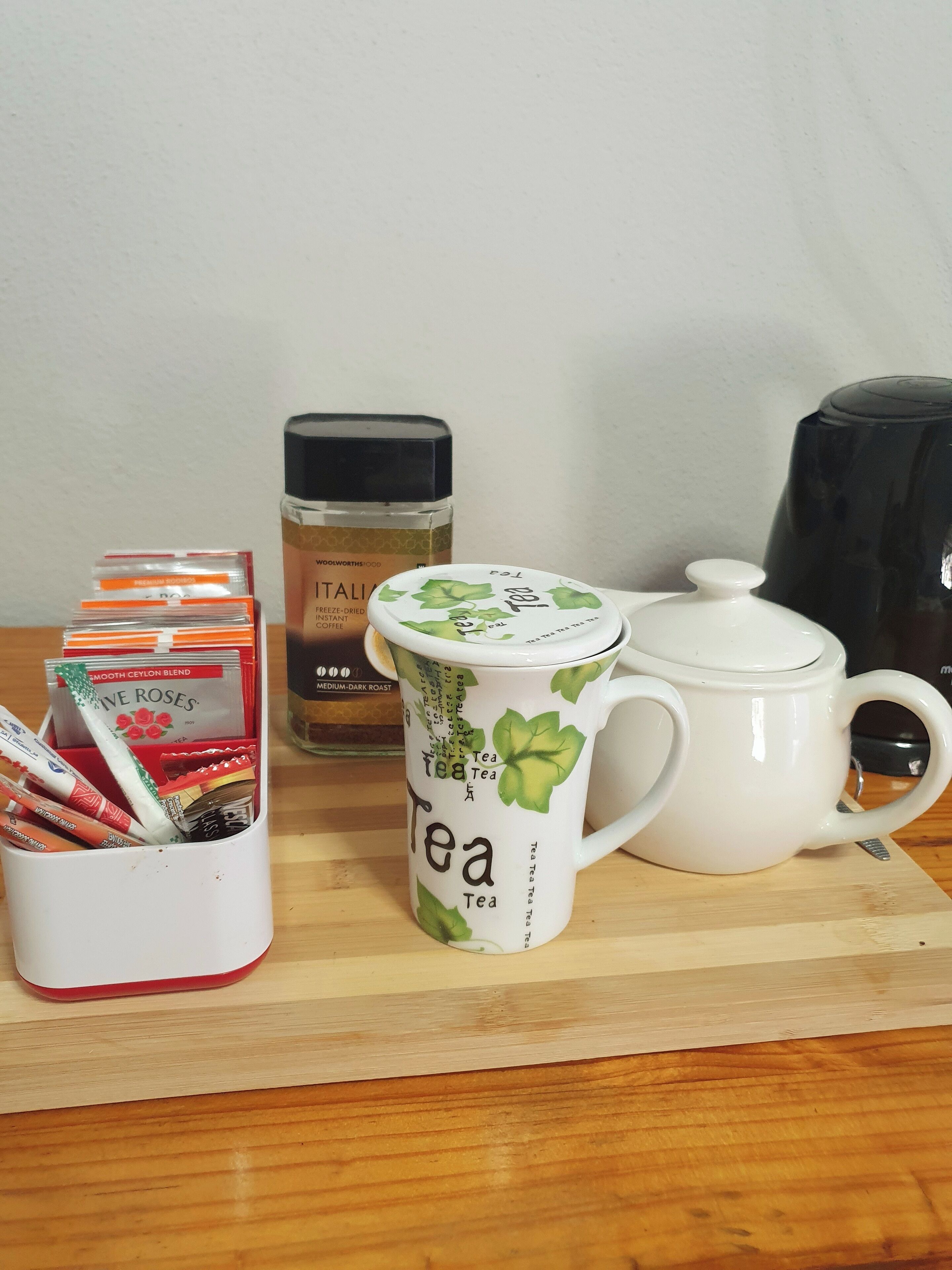 A tea setup with a mug, teapot, and packets on a wooden board.