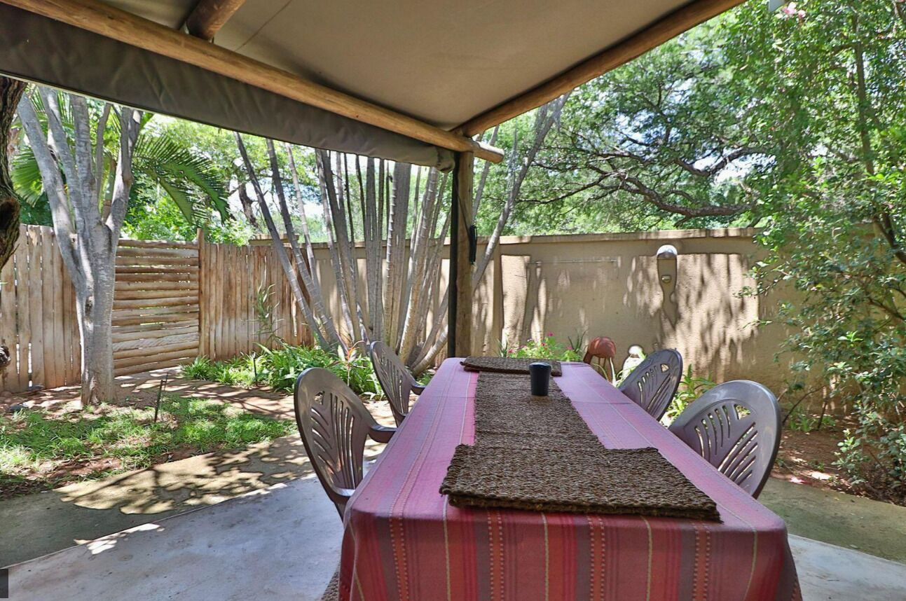 Un patio exterior con una mesa lista para dos personas, rodeado de sillas, bajo una pérgola de madera.