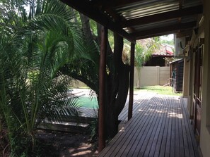 A wooden deck with a covered area, surrounded by lush greenery and a pool. - Gecko Cottage (Nkomazi)