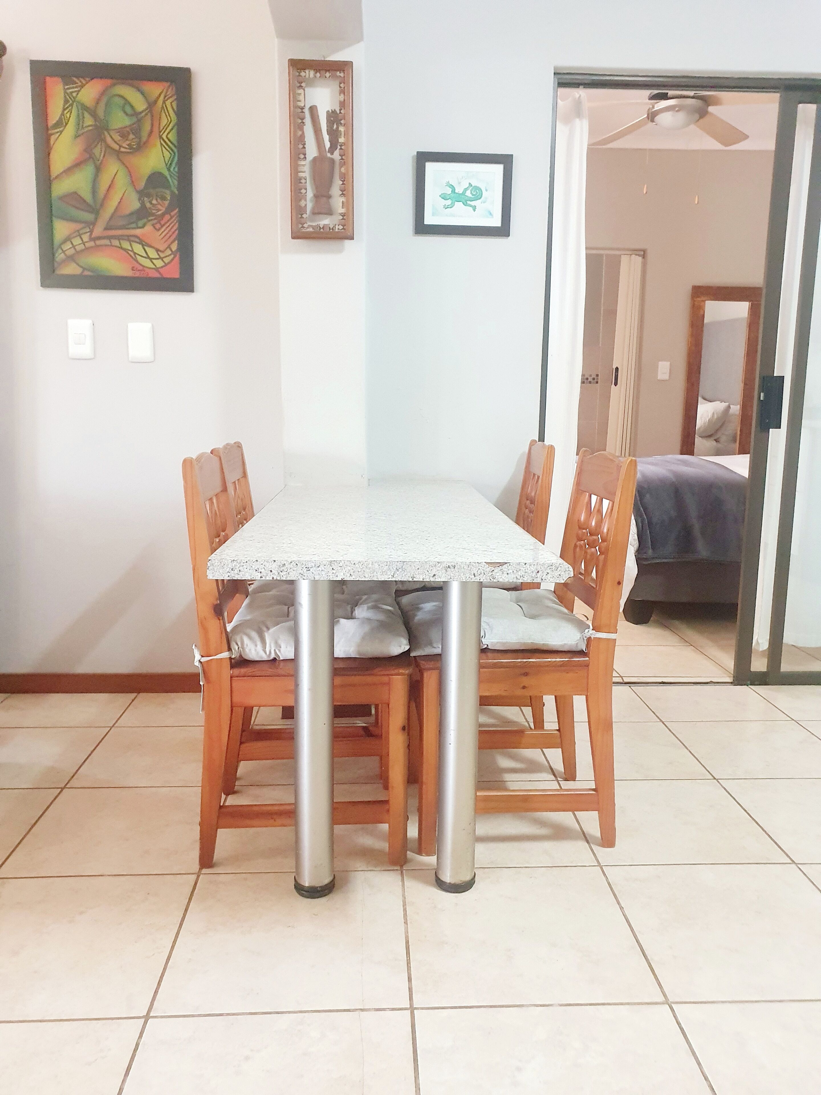 Un comedor con mesa y sillas, un ventilador de techo y una cama al fondo.