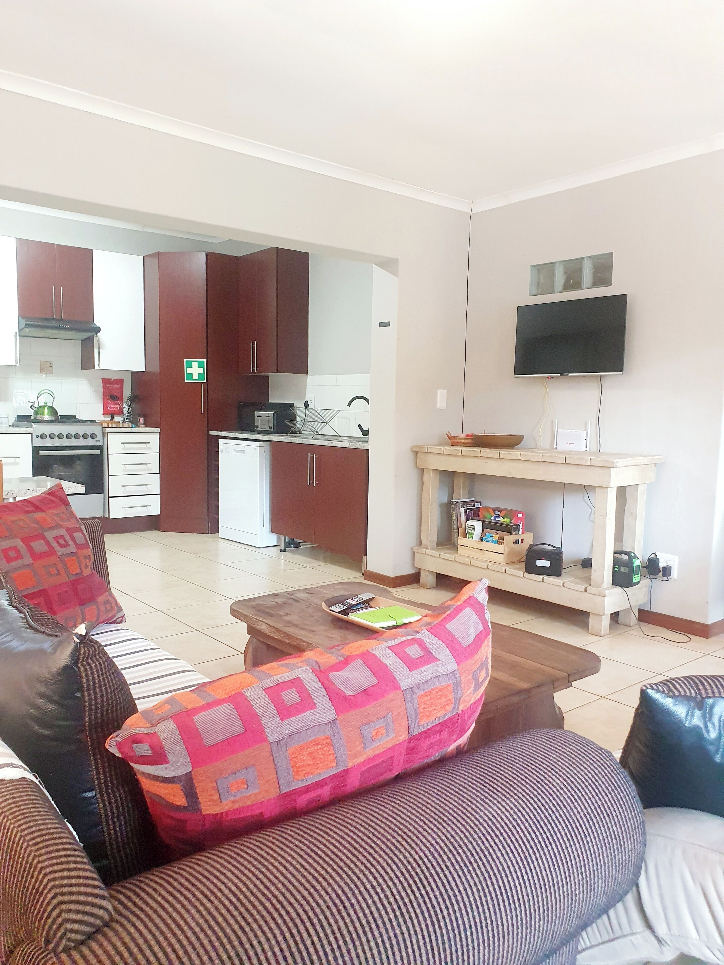 Una sala de estar con sofá, mesa de centro y televisión. Se observa una cocina al fondo, con armarios y electrodomésticos.