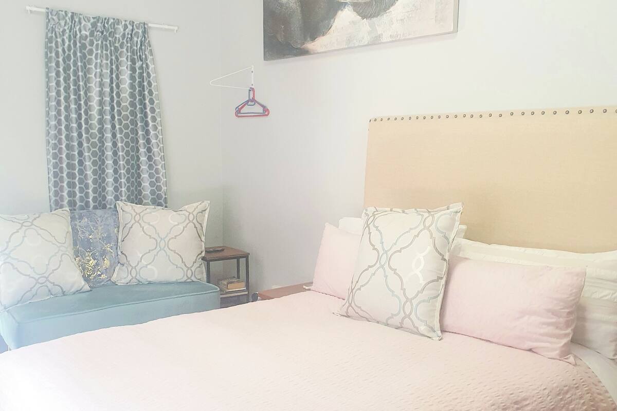 A bedroom with a large bed, a headboard, a wall-mounted artwork, a bedside table, and a hanging light.