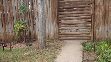A concrete pathway leading to a wooden gate, surrounded by a wooden fence, with various plants and trees.