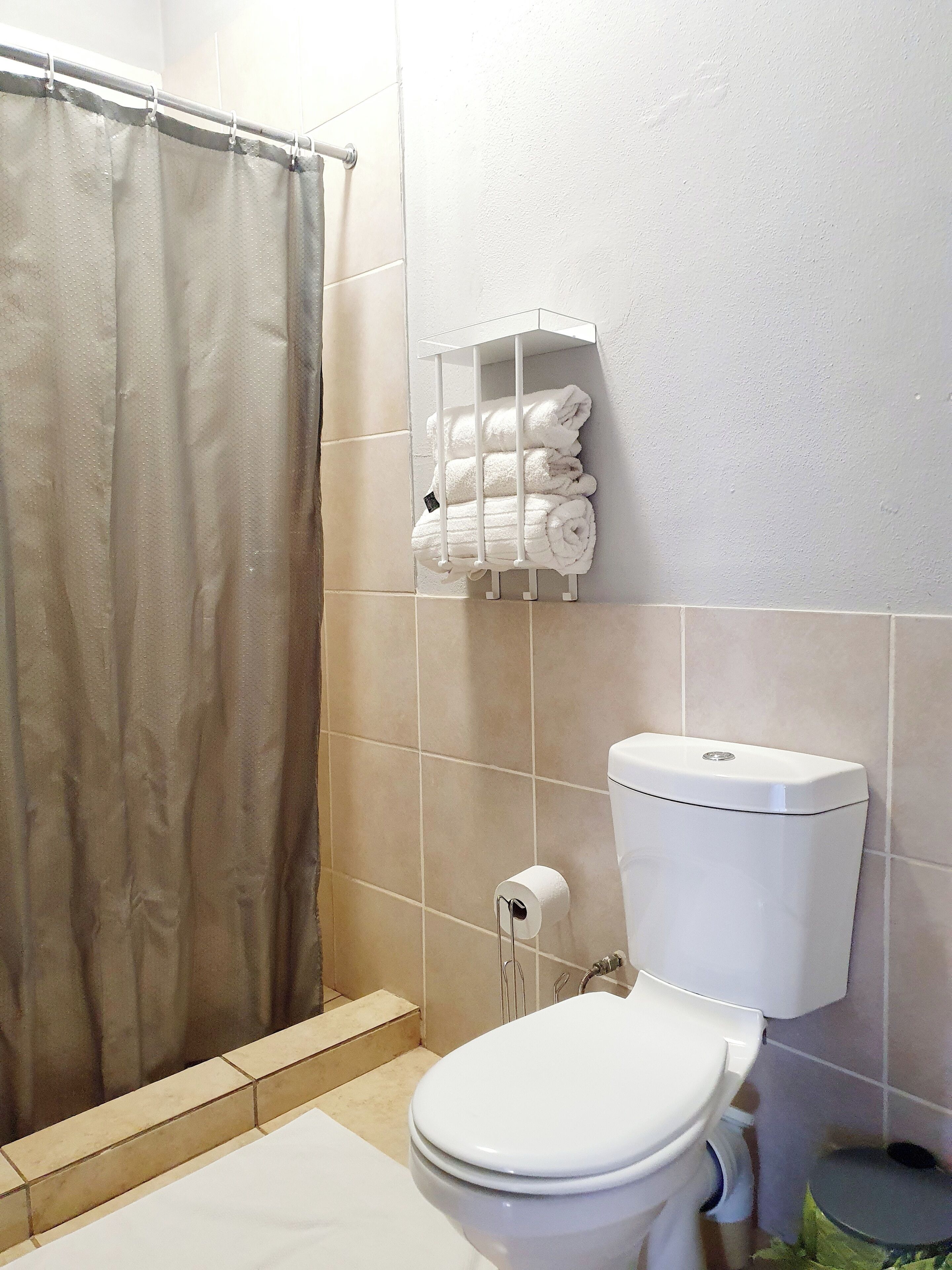 A bathroom with a toilet, a towel rack with folded towels, a shower curtain, and a toilet paper holder.