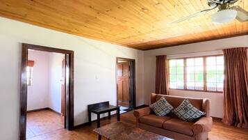 A room with wooden flooring, a brown sofa with patterned cushions, a small table, and a ceiling fan.