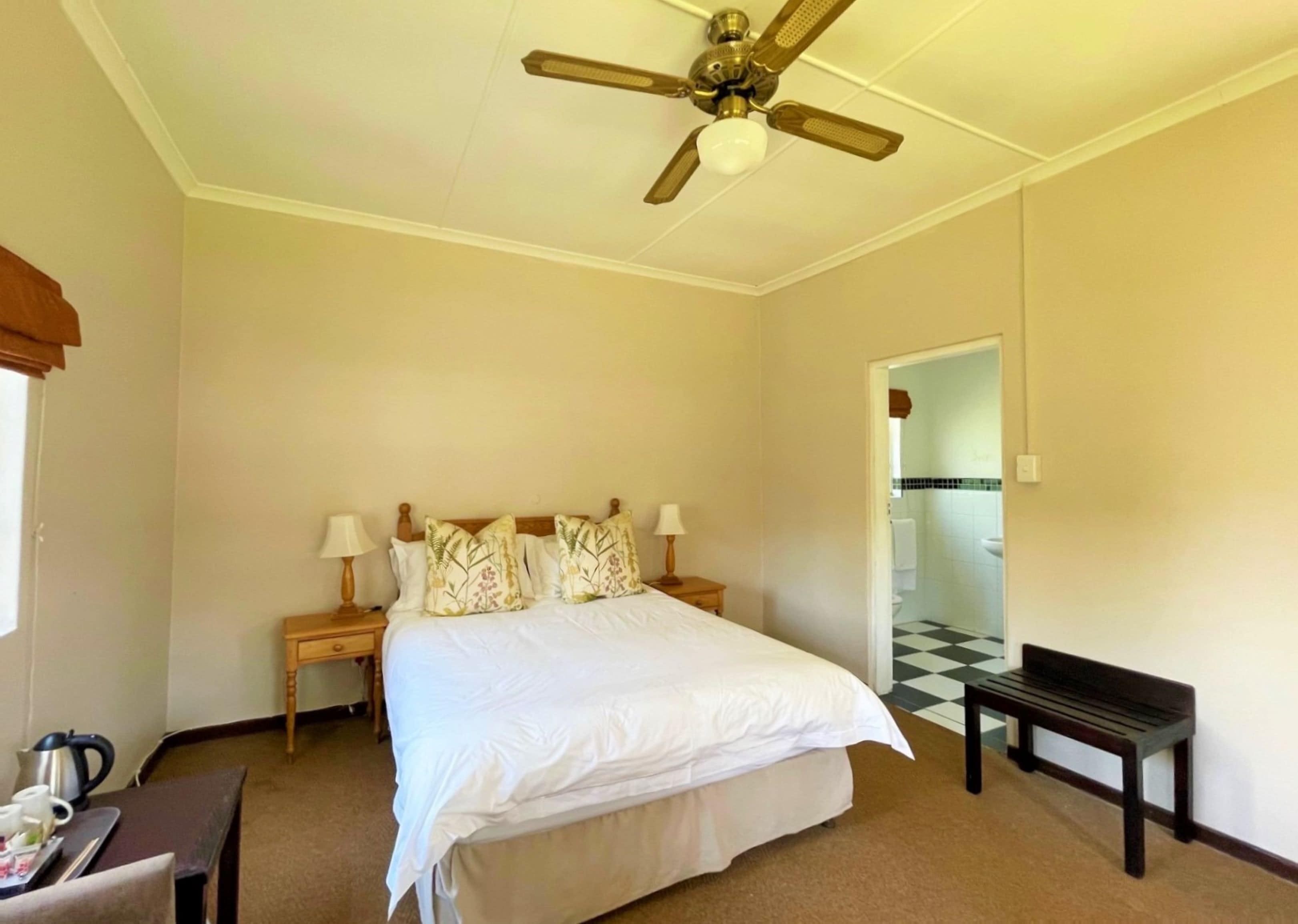Una habitación de hotel con cama, mesitas de noche, un banco, ventilador de techo y suelo a cuadros.
