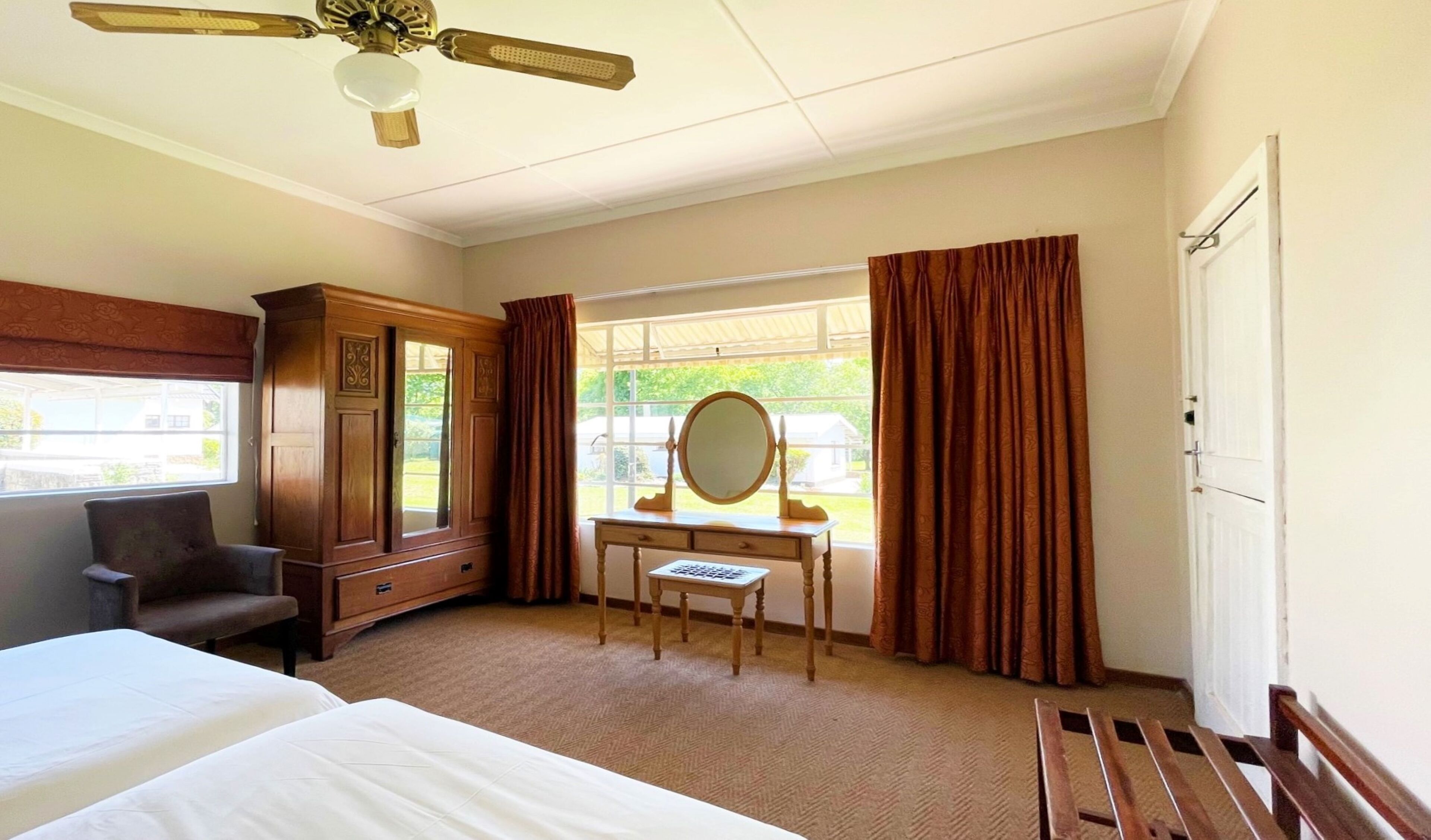 Ein Hotelzimmer mit Bett, Schreibtisch mit Spiegel, Stuhl, Kleiderschrank und einem Fenster mit Vorhängen.