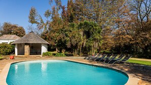Piscina com estrutura de telhado de palha e espreguiçadeiras.