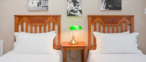 A twin room with two wooden beds, a green desk lamp, and three framed pictures on the wall.