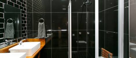 A modern bathroom with a glass-enclosed shower, a wooden vanity with two sinks, and a mirror with two towels.