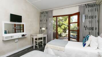 A hotel room with two beds, a desk, a chair, a TV, and a sliding glass door to the outside.