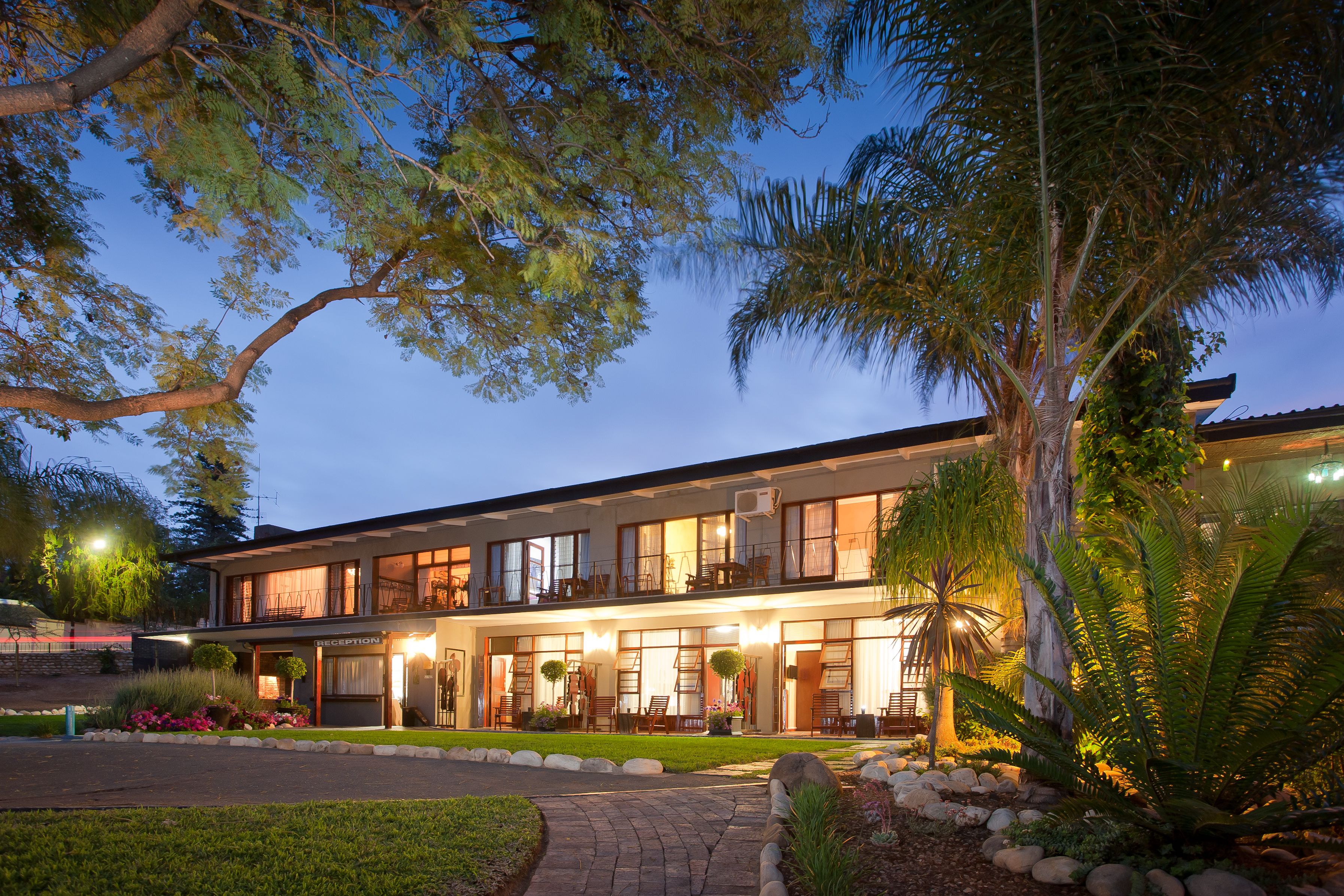 A two-story hotel with a reception area, outdoor seating, and a well-maintained garden.