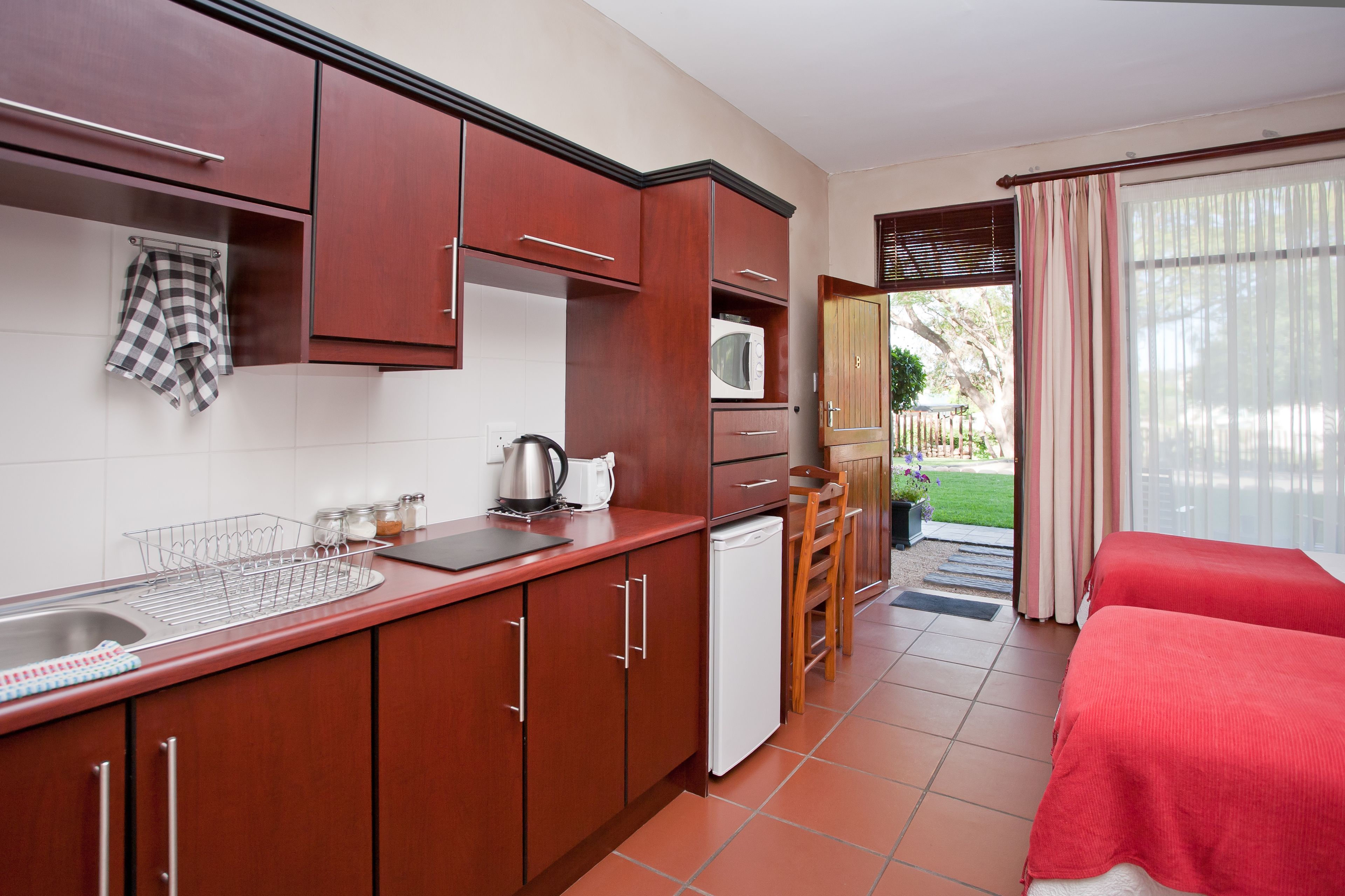 Una cocina compacta con pileta, microondas y refrigerador. Hay un pequeño comedor con mesa y sillas, y un balcón con vista al exterior.