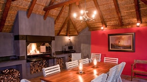 Un coin repas avec une table en bois et des chaises blanches, une cheminée et un mur rouge orné d’un tableau encadré.