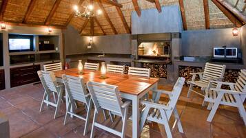 Una cocina al aire libre con zona de comedor, que incluye una mesa, sillas, un televisor y una chimenea.