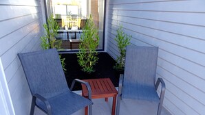 Uma pequena área externa com assento, incluindo duas cadeiras e uma mesa, cercada por paredes de revestimento branco e plantas em vasos.