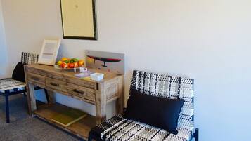 A room with a wooden desk, a framed certificate, a fruit bowl, a chair with a patterned cushion, and a wall-mounted picture.